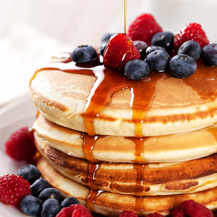 Une pile de crAapes garnie de bleuets frais, de framboises et de sirop d'ACrable.