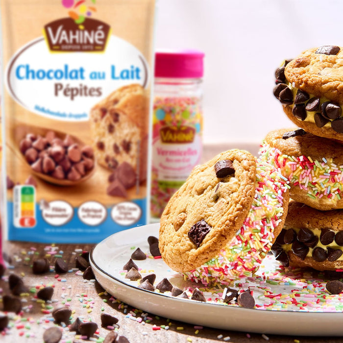 Cette image présente des pépites de chocolat au lait Vahiné à côté de biscuits colorés recouverts de vermicelles, mettant en évidence les ingrédients de pâtisserie et les friandises finies.