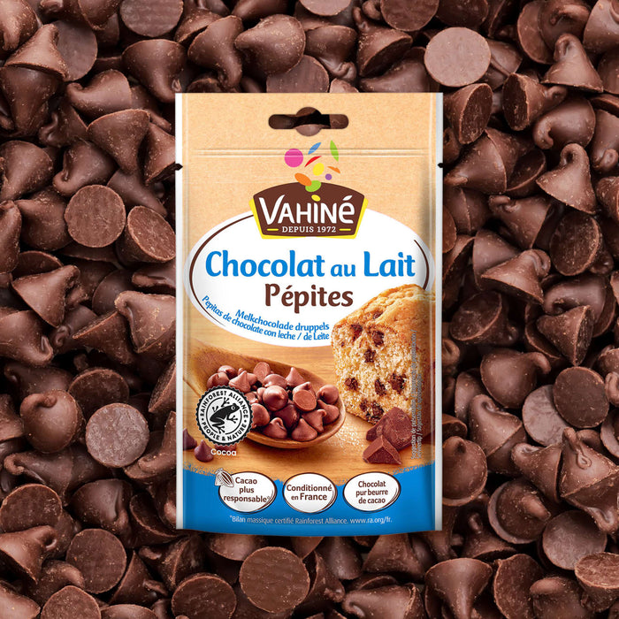 Un paquet de Vahine Sch Pepites Chocolaitx10-Va, présentant des Pépites de Chocolat au Lait Vahiné, est affiché sur un fond de pépites de chocolat au lait éparpillées.