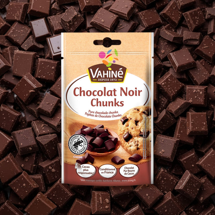 Un emballage de la marque Vahiné de Vahine Sch100G Pepites Chunkx10-Va, affichant le texte Chocolat Noir Chunks et une image de pépites de chocolat et d'un cookie, est présenté sur un fond de morceaux de chocolat noir éparpillés.