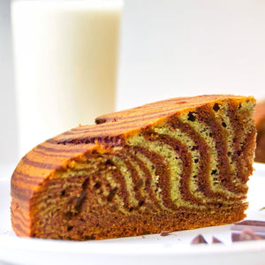 Une tranche de gActeau zACbrAC avec des couches distinctes de chocolat et de vanille repose sur une assiette blanche, accompagnACe d'un verre de lait.