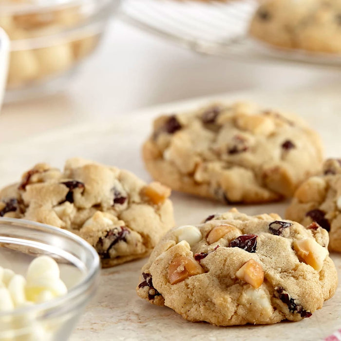 Gros plan sur des biscuits fraARchement cuits avec des pACpites de chocolat blanc, des canneberges et des morceaux de caramel.