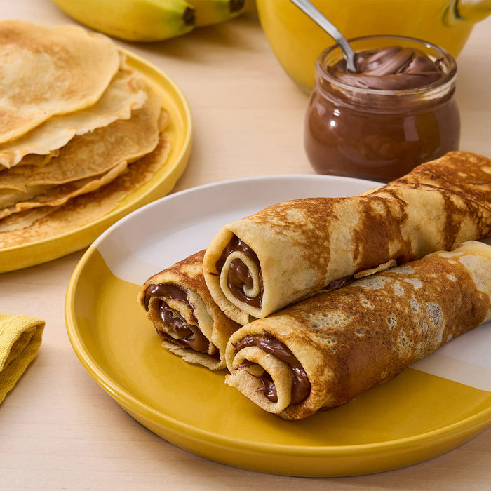 Une assiette de crAapes fourrACes au Nutella, A? cA?tAC d'une pile de crAapes nature, d'un pot de Nutella et de bananes.
