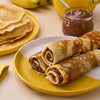 Une assiette de crAapes fourrACes au Nutella, A? cA?tAC d'une pile de crAapes nature, d'un pot de Nutella et de bananes.