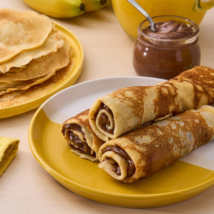 Une assiette de crAapes fourrACes au Nutella, A? cA?tAC d'une pile de crAapes nature, d'un pot de Nutella et de bananes.