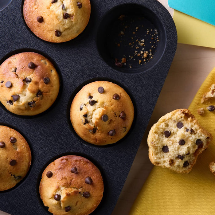 Un moule A? muffins rempli de muffins aux pACpites de chocolat fraARchement cuits, un muffin est coupAC en deux pour montrer la texture intACrieure.