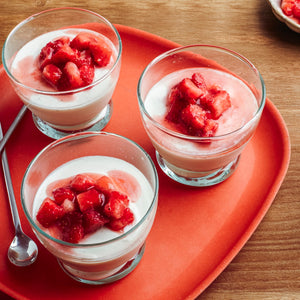 Trois verres de panna cotta garnis de fraises fraîches sont posés sur un plateau orange vif.