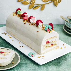 Une bûche de Noël festive décorée de personnages de fêtes et d'un glaçage blanc brillant, posée sur un plat blanc.
