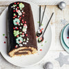 Une bûche de Noël festive au chocolat, décorée de décorations sur le thème des fêtes, est posée sur une assiette blanche, transmettant un sentiment de célébration et de gourmandise.