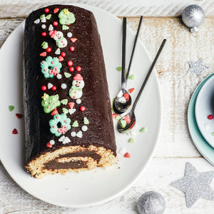 Une bûche de Noël festive au chocolat, décorée de décorations sur le thème des fêtes, est posée sur une assiette blanche, transmettant un sentiment de célébration et de gourmandise.