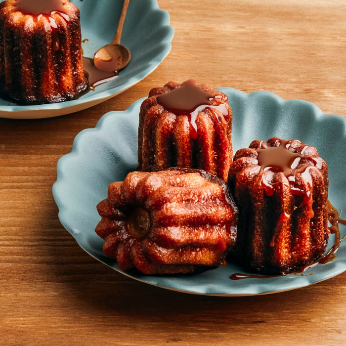 Trois cannelés sont disposés sur une assiette bleue avec un aspect brillant et caramélisé.