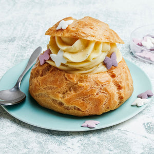 Un chou à la crème rempli de crème pâtissière et décoré de confettis papillons est posé sur une assiette bleu clair.