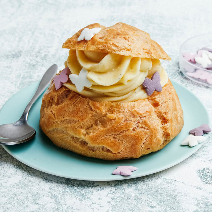 Un chou à la crème rempli de crème pâtissière et décoré de confettis papillons est posé sur une assiette bleu clair.