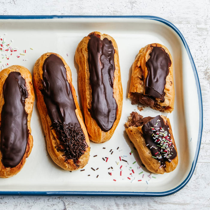 Un plateau d'éclairs au chocolat, certains décorés de vermicelles, présentant une délicieuse option de dessert.