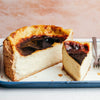 Une part de gâteau au fromage basque brûlé est posée à côté du reste du gâteau sur une assiette à bord bleu, mettant en valeur son dessus caramélisé et son intérieur crémeux.