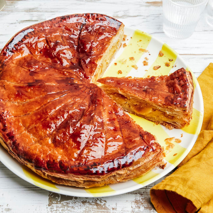 Une Galette des Rois dorée, une galette traditionnelle française, est présentée sur une assiette colorée avec une part coupée.