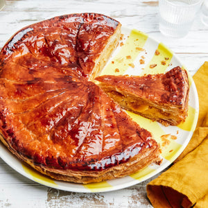 Une Galette des Rois dorée, une galette traditionnelle française, est présentée sur une assiette colorée avec une part coupée.