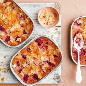 Trois petits gâteaux rectangulaires aux framboises et aux amandes sont présentés sur une planche en bois avec un bol d'amandes effilées.