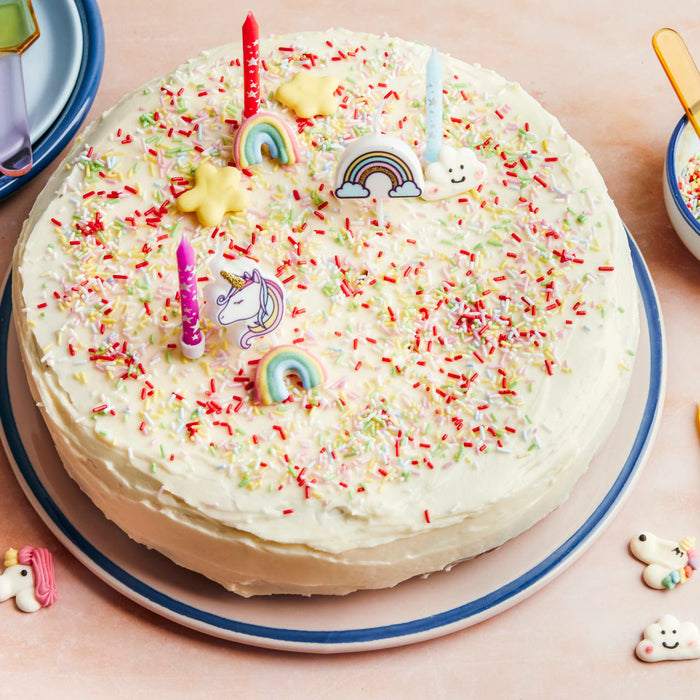Un gâteau d'anniversaire festif décoré de vermicelles, de bougies et de décorations fantaisistes de licorne et d'arc-en-ciel.