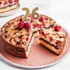Un gâteau aux framboises et aux amandes avec une couche de chocolat est décoré d'une bougie numéro 26, suggérant une célébration d'anniversaire.