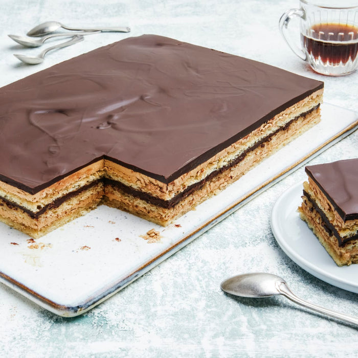 Une part est coupée d'un gâteau Dobos rectangulaire, révélant son gâteau à étages et sa ganache au chocolat.