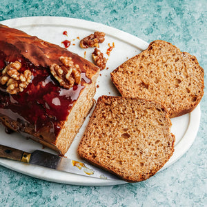 Un cake glacé aux noix, présenté sur un plateau blanc avec deux tranches coupées et un couteau à côté.