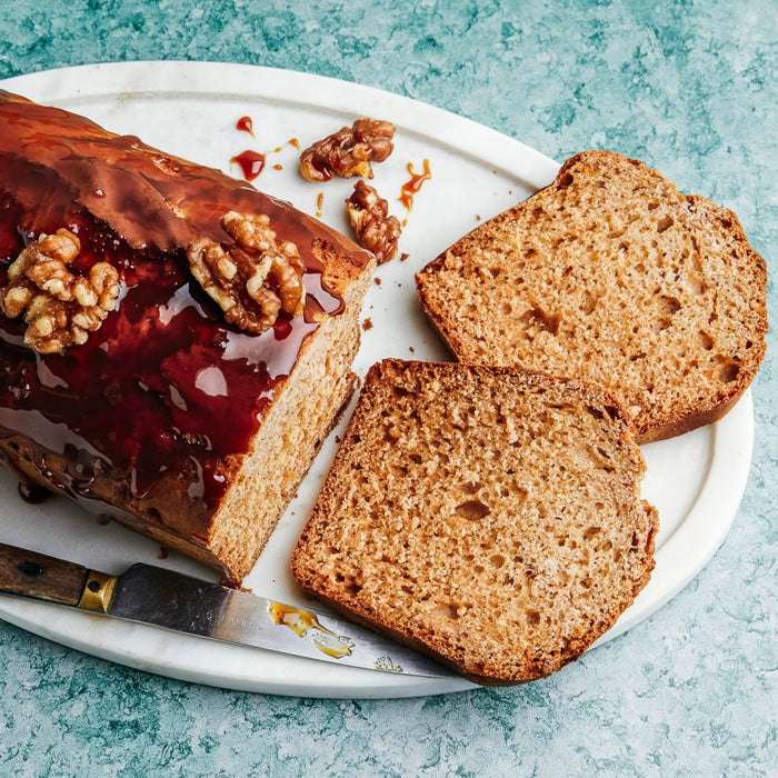 Un cake glacé aux noix, présenté sur un plateau blanc avec deux tranches coupées et un couteau à côté.