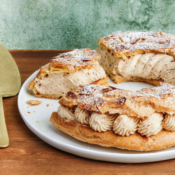 Un Paris-Brest tranché, saupoudré de sucre glace, présente sa garniture à la crème sur une assiette blanche.