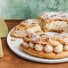 Un Paris-Brest tranché, saupoudré de sucre glace, présente sa garniture à la crème sur une assiette blanche.