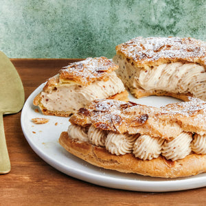 Un Paris-Brest tranché, saupoudré de sucre glace, présente sa garniture à la crème sur une assiette blanche.