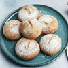 Une assiette de six petits pains ronds, dorés, saupoudrés de sucre glace, chacun avec une petite fente sur le dessus.