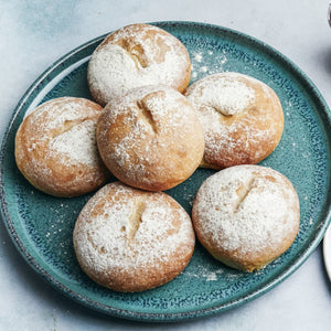Une assiette de six petits pains ronds, dorés, saupoudrés de sucre glace, chacun avec une petite fente sur le dessus.