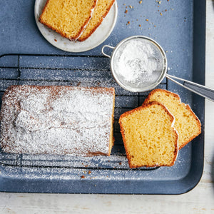 Un cake fraîchement cuit, saupoudré de sucre glace, repose sur une grille à pâtisserie à côté de tranches coupées, suggérant une gourmandise faite maison.