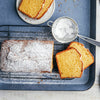 Un cake fraîchement cuit, saupoudré de sucre glace, repose sur une grille à pâtisserie à côté de tranches coupées, suggérant une gourmandise faite maison.