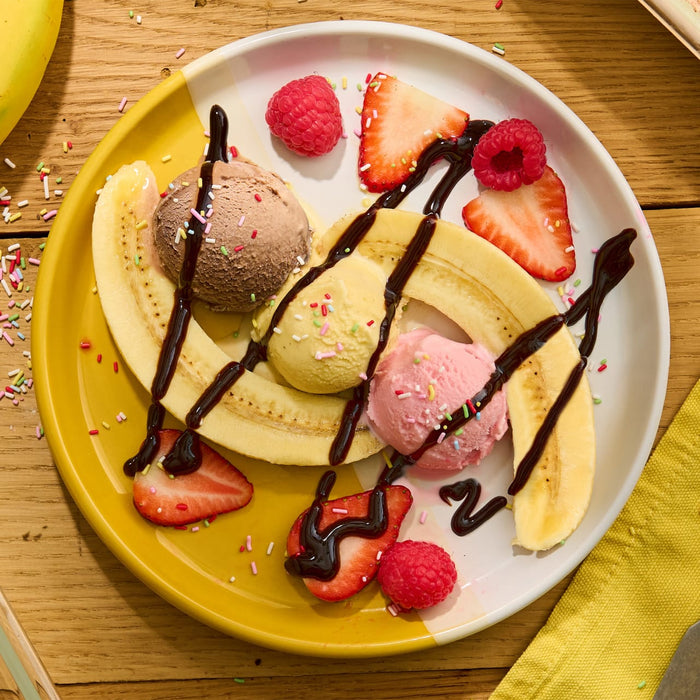 Un dessert banana split coloré avec des boules de glace, sauce au chocolat, fraises et framboises.