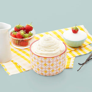 Un bol de crème à la vanille est présenté avec des fraises fraîches et des gousses de vanille, suggérant un délicieux dessert.