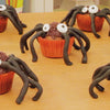 Un groupe de cupcakes araignées d'Halloween avec glaçage au chocolat, yeux en bonbons et pattes en réglisse noire sont disposés sur une table.