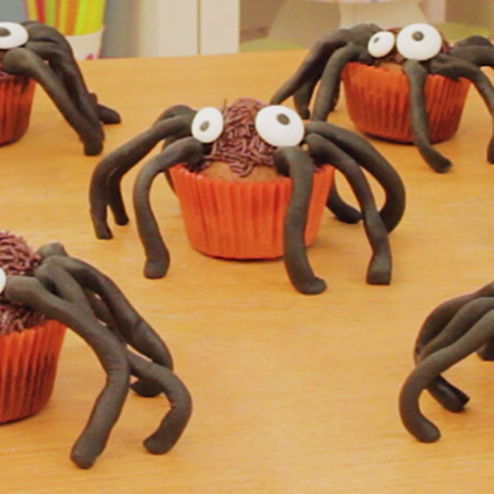 Un groupe de cupcakes araignées d'Halloween avec glaçage au chocolat, yeux en bonbons et pattes en réglisse noire sont disposés sur une table.