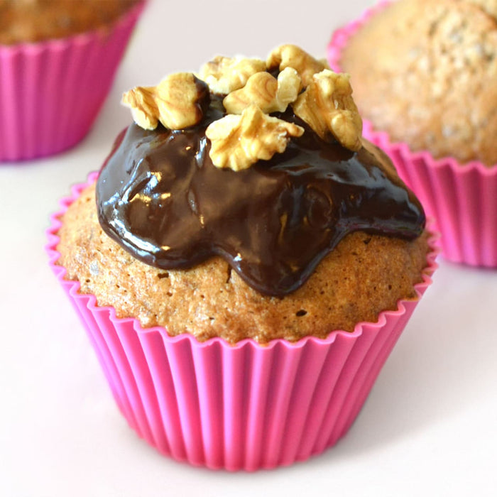Un délicieux muffin dans un moule en silicone rose est garni de glaçage au chocolat et de noix.