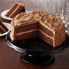 Un délicieux gâteau au chocolat à deux étages avec glaçage au chocolat est présenté sur un présentoir à gâteau noir, avec deux parts déjà coupées et servies.