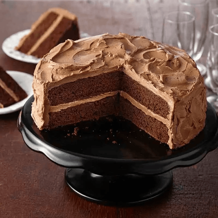 Un délicieux gâteau au chocolat à deux étages avec glaçage au chocolat est présenté sur un présentoir à gâteau noir, avec deux parts déjà coupées et servies.