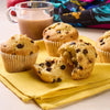 Un groupe de muffins aux pépites de chocolat sont disposés sur une serviette jaune à côté d'un verre de lait chocolaté, suggérant un délicieux petit-déjeuner ou une collation.