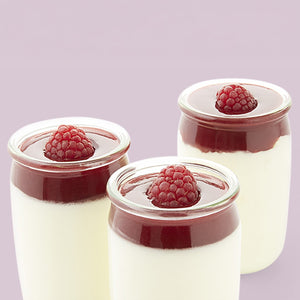 Trois petits pots en verre remplis d'un dessert crémeux, nappés d'une sauce aux fruits rouges et d'une framboise.
