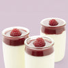Trois petits pots en verre remplis d'un dessert crémeux, nappés d'une sauce aux fruits rouges et d'une framboise.