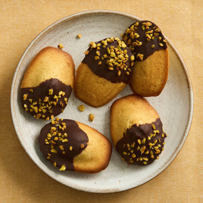 Une assiette de madeleines trempées dans le chocolat et saupoudrées de pistaches.