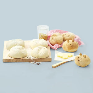 Une sélection de petits pains fraîchement cuits, certains en forme de lapins, disposés sur une planche en bois et un tissu rose à pois.