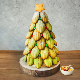 Un arbre de NoA<l fait de madeleines dACcorACes de bonbons, surmontAC d'un biscuit ACtoile, posAC sur une base en bois.