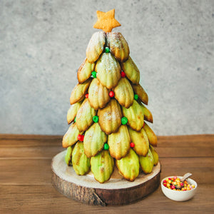 Un arbre de NoA<l fait de madeleines dACcorACes de bonbons, surmontAC d'un biscuit ACtoile, posAC sur une base en bois.