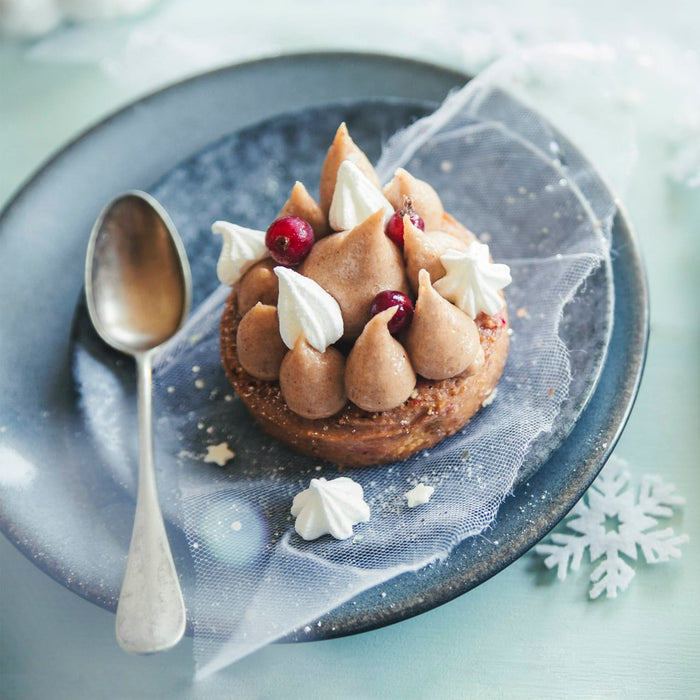 Une délicieuse tarte aux châtaignes est présentée sur une assiette grise, ornée de meringues et d'airelles, suggérant un dessert festif.