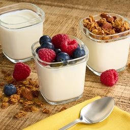Trois petits récipients en verre remplis de yaourt, un nature, un aux baies et un au granola, présentant une option de petit-déjeuner ou de collation saine.